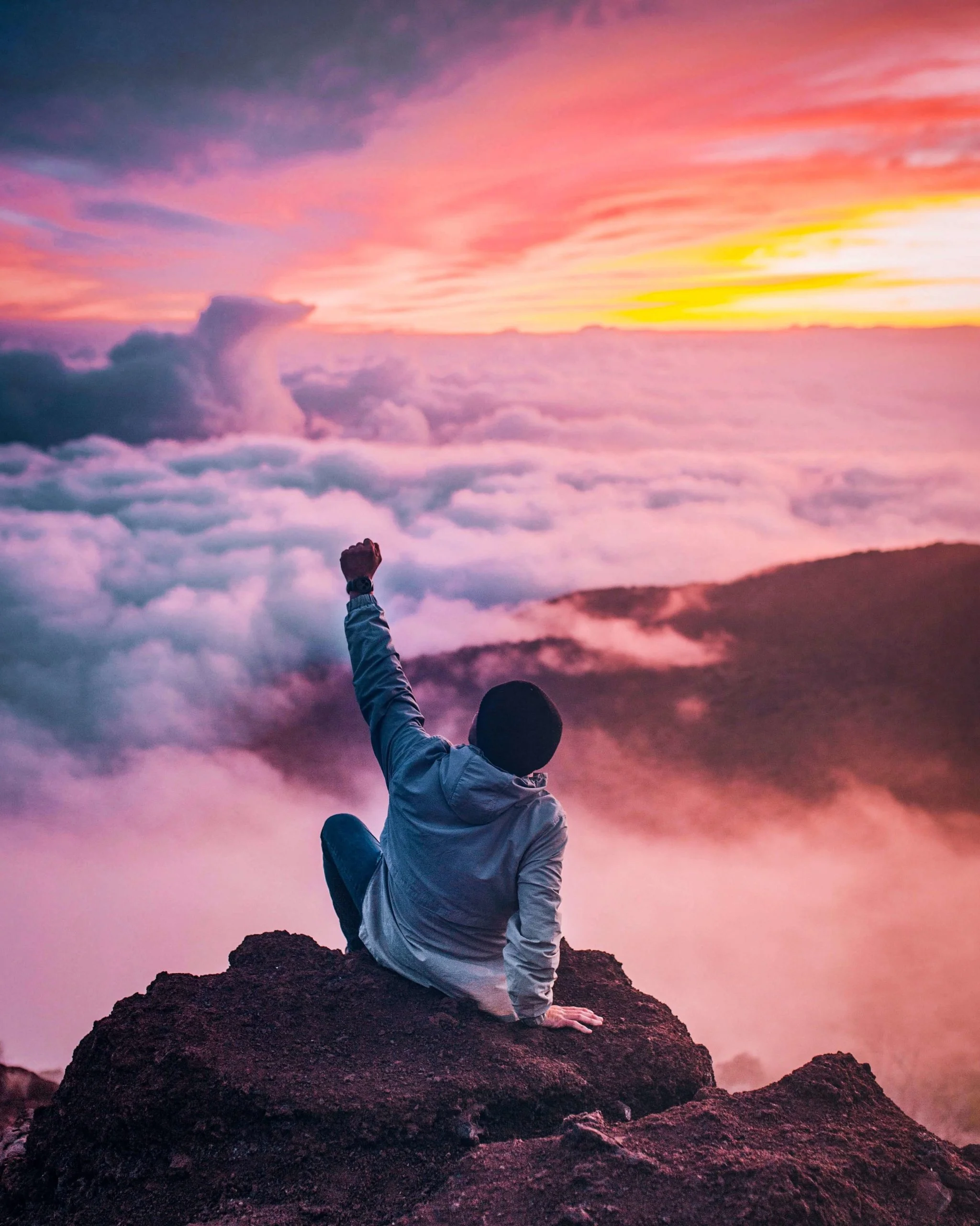 personne au sommet d'une montagne le poing levé vers le ciel au coucher du soleil