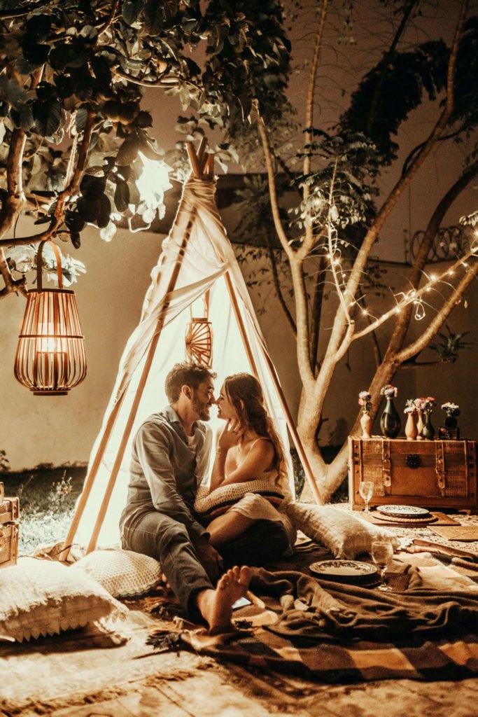couple se regardant tendrement dans un setting avec une tente, des couvertures et des lumignons