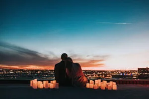 couple assis entre des bougies sur un toit regardant les lumières de la ville au soleil couchant
