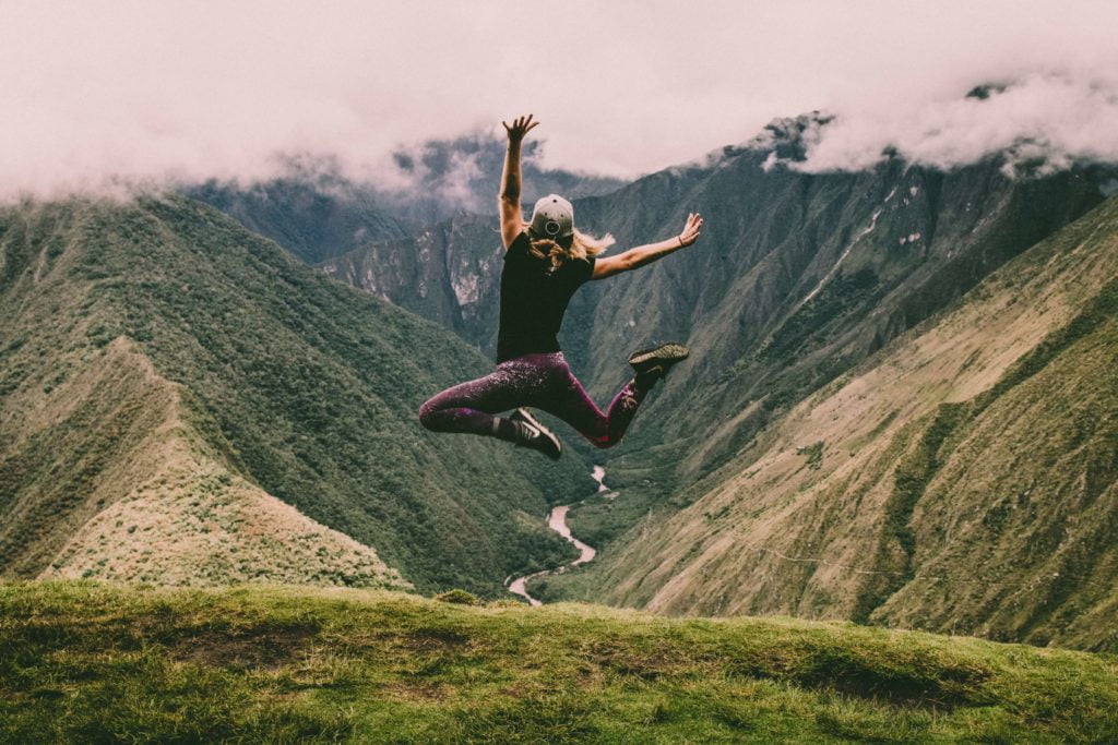 Femme sautant en l'air face à une vallée verdoyante
